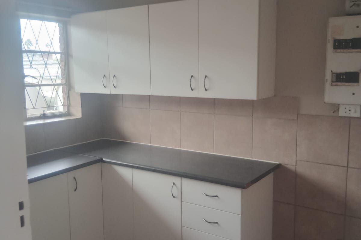 A functional kitchen area featuring white cabinetry, dark countertops, tiled splashbacks, and tiled flooring.