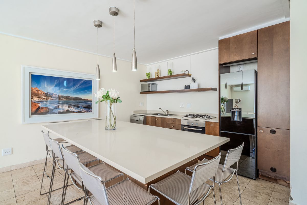 Modern kitchen featuring a large stone island, built-in oven, gas hob, and ample wooden cabinetry with floating shelves.