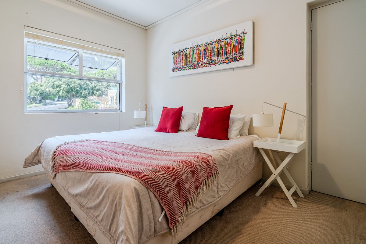A bright bedroom featuring neutral carpet flooring and a large sliding window providing natural light and a view of the surrounding greenery.