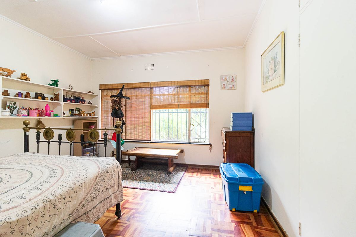 A bedroom featuring parquet flooring, built-in shelving, and a window fitted with security bars and bamboo blinds.