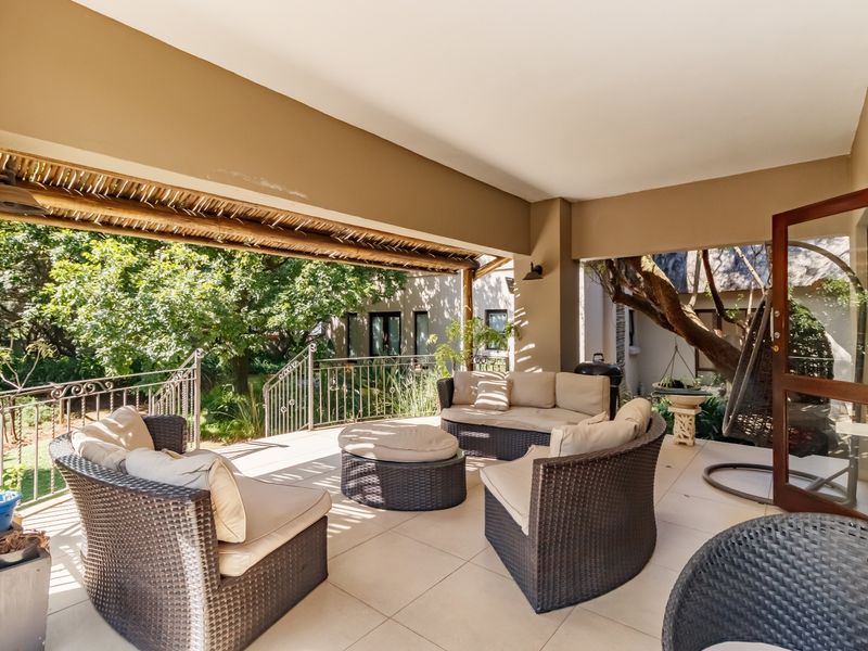 A spacious covered patio featuring tiled flooring, a thatched roof section, and wrought iron railings, overlooking a lush garden area.