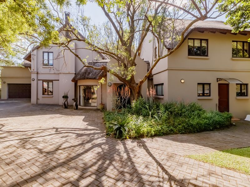 A well-maintained front exterior view of a house featuring a thatched roof, paved driveway, and established garden landscaping.