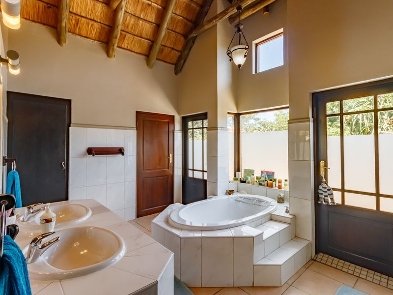 Spacious bathroom featuring a double vanity, built-in bathtub, and high vaulted ceilings with exposed timber rafters and thatch detailing.