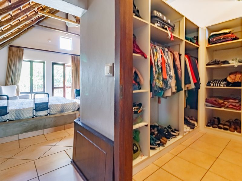 A bedroom featuring a walk-in closet with built-in shelving, tiled flooring, and exposed timber rafters under a pitched roof.