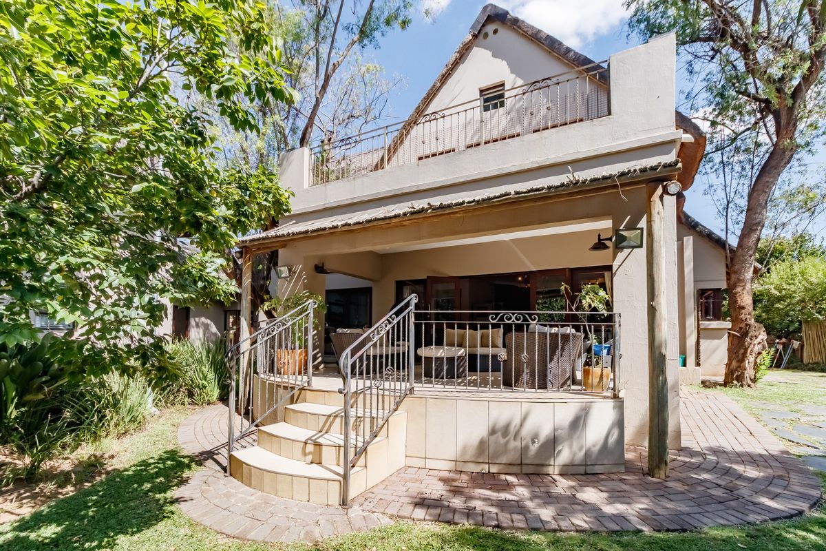 Rear view of the property featuring a covered patio, elevated balcony with wrought iron railings, and a paved garden walkway.