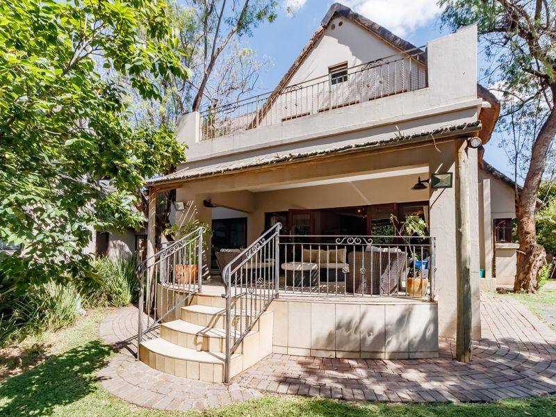 Rear view of the property featuring a covered patio, elevated balcony with wrought iron railings, and a paved garden walkway.