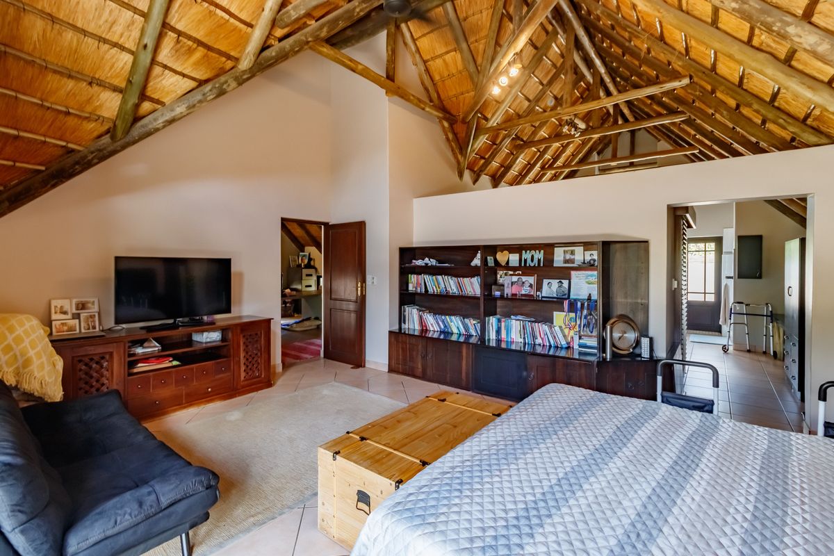 Spacious bedroom featuring a high vaulted thatch ceiling with exposed timber beams, tiled flooring, and integrated wooden storage cabinetry.
