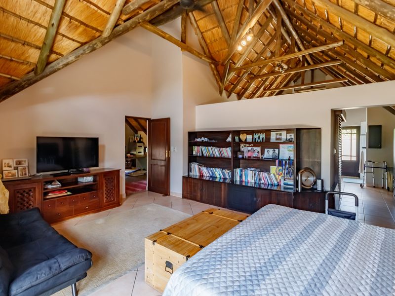 Spacious bedroom featuring a high vaulted thatch ceiling with exposed timber beams, tiled flooring, and integrated wooden storage cabinetry.