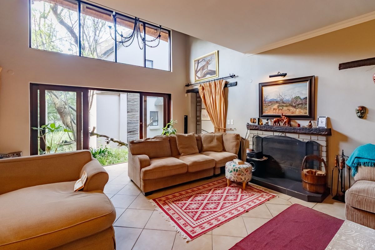 Spacious living room featuring high ceilings, large windows, tiled flooring, and a built-in fireplace, offering a bright and airy atmosphere with garden access.
