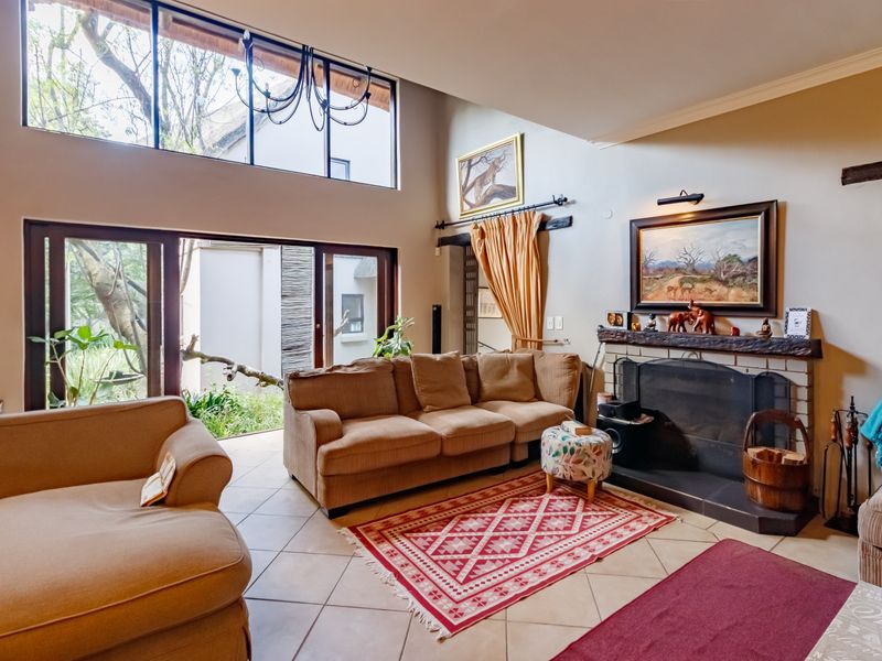 Spacious living room featuring high ceilings, large windows, tiled flooring, and a built-in fireplace, offering a bright and airy atmosphere with garden access.