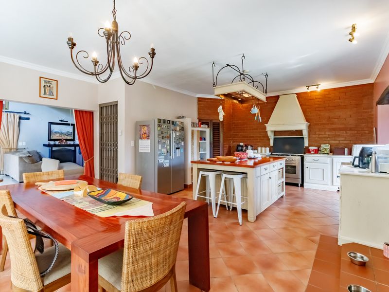 Spacious open-plan kitchen and dining area featuring terracotta flooring, an exposed brick feature wall, a central kitchen island, and a classic wrought iron chandelier.