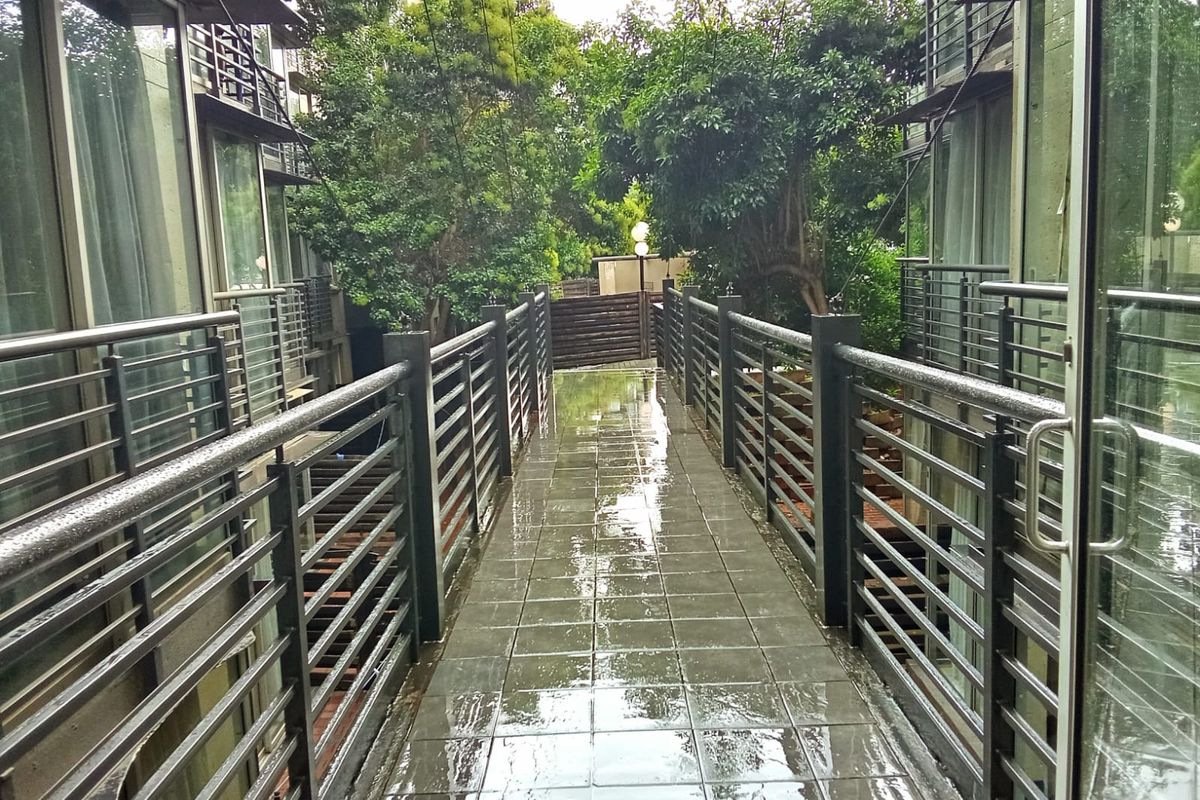 A covered walkway or bridge featuring tiled flooring and metal railings, connecting sections of the apartment complex amidst lush greenery.