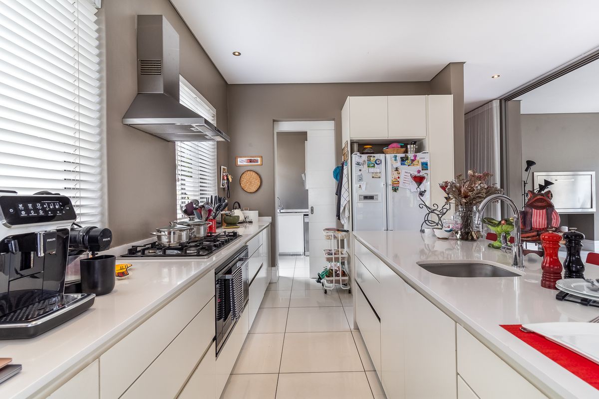 Modern kitchen featuring sleek white cabinetry, stone countertops, a gas hob, stainless steel extractor fan, and a central island with an integrated sink.