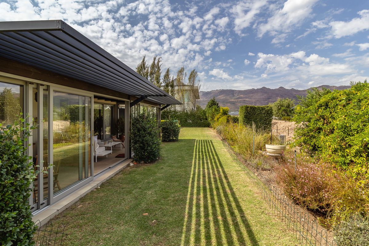 A well-maintained rear garden featuring a manicured lawn, established landscaping, and a covered patio area with large sliding glass doors.