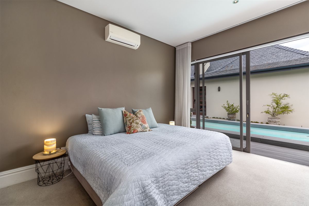 Spacious bedroom featuring neutral carpeting, wall-mounted air conditioning unit, and large sliding glass doors providing direct access to the outdoor pool area.