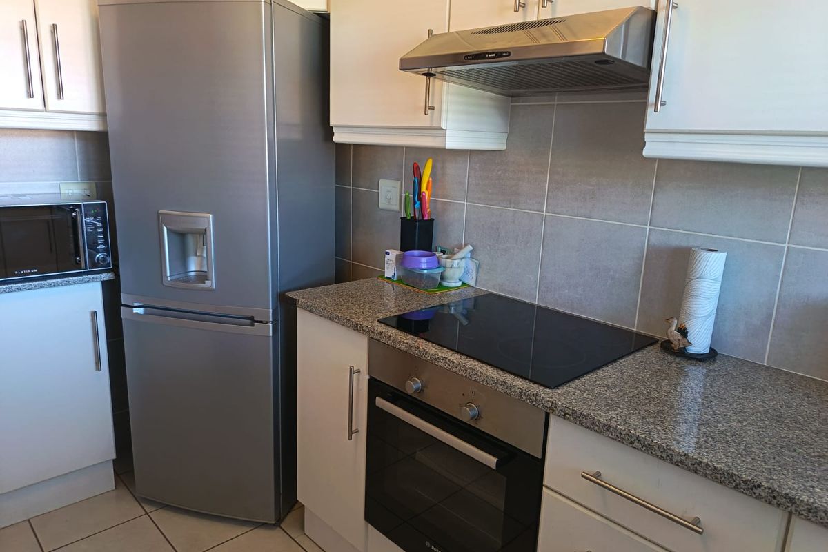 A functional kitchen featuring granite countertops, built-in oven, electric hob, extractor fan, and ample cabinetry with tiled backsplash and flooring.