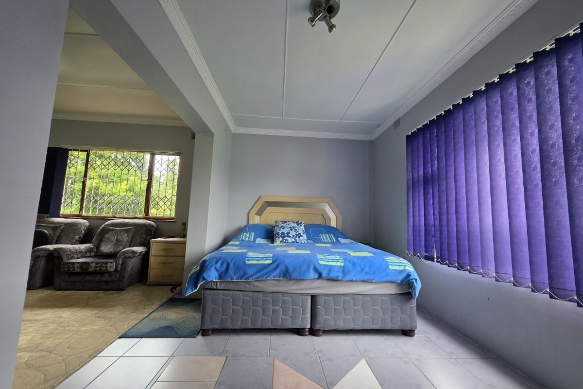 A bedroom featuring tiled flooring, ceiling cornicing, and security bars on the windows, with an adjacent seating area visible.