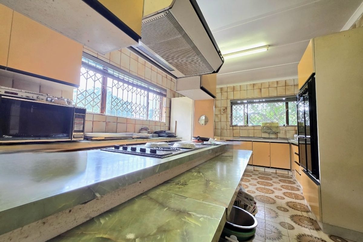 A spacious, dated kitchen featuring extensive cabinetry, built-in oven and hob, and large windows with security bars, offering significant potential for modernization.