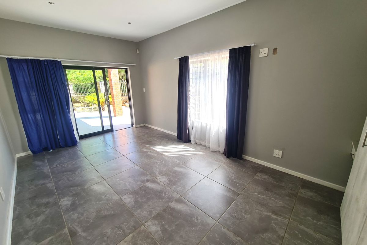 A bright, empty living room featuring large format grey floor tiles, recessed lighting, and a sliding glass door providing access to the outdoor area.
