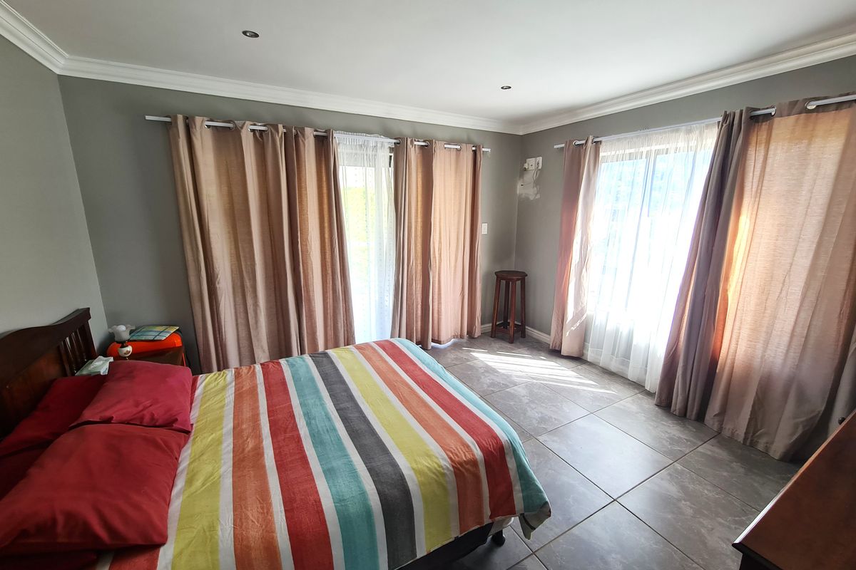 Spacious bedroom featuring large windows with curtains, tiled flooring, and recessed lighting, offering direct access to the outdoors via a sliding glass door.
