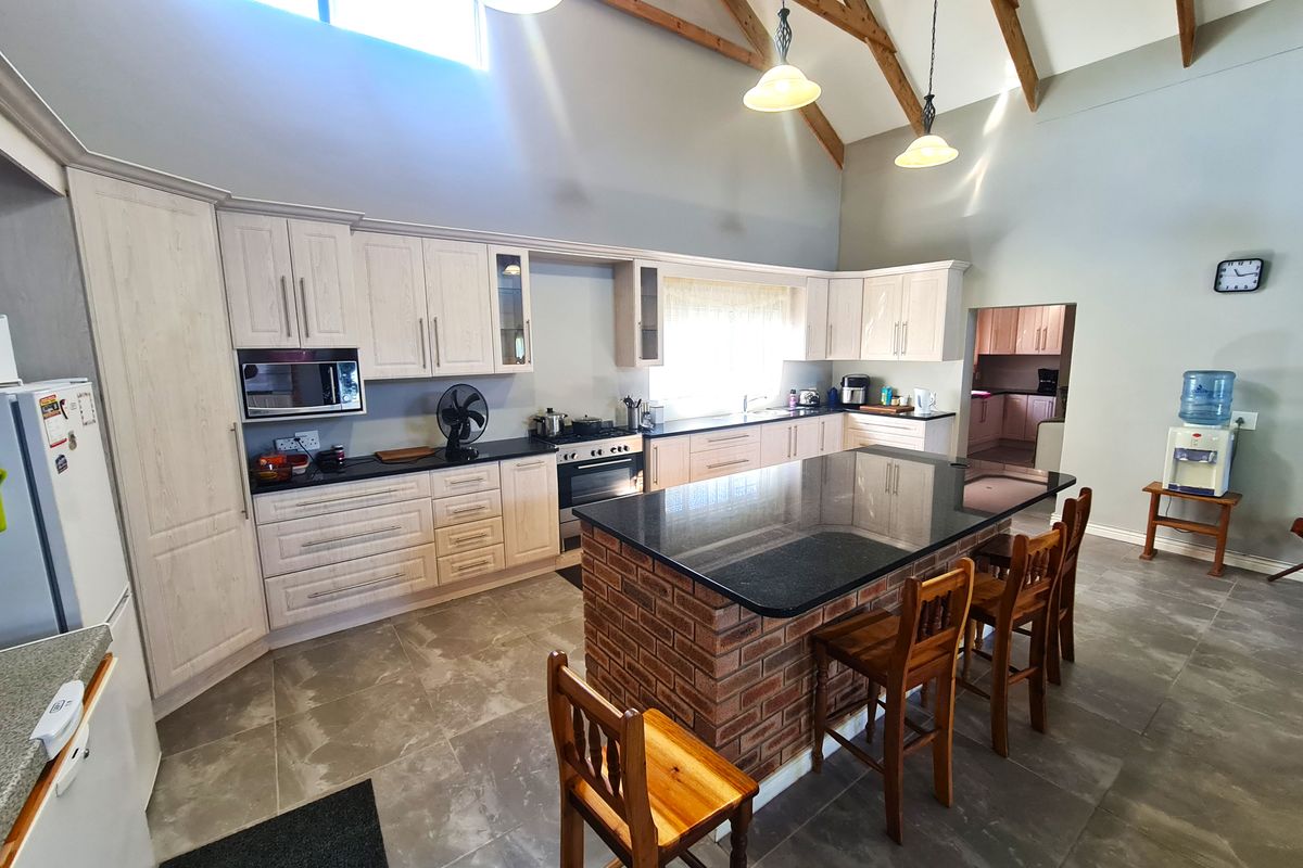 Spacious kitchen featuring a brick-base island with granite countertops, light wood cabinetry, vaulted ceilings with exposed timber trusses, and tiled flooring.