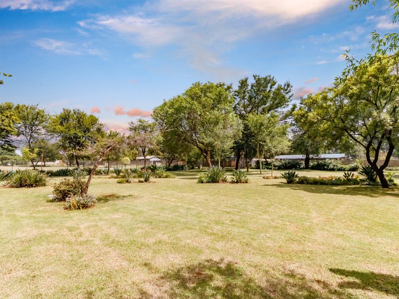 A spacious, well-maintained garden featuring mature trees, established landscaping, and a large open lawn area.