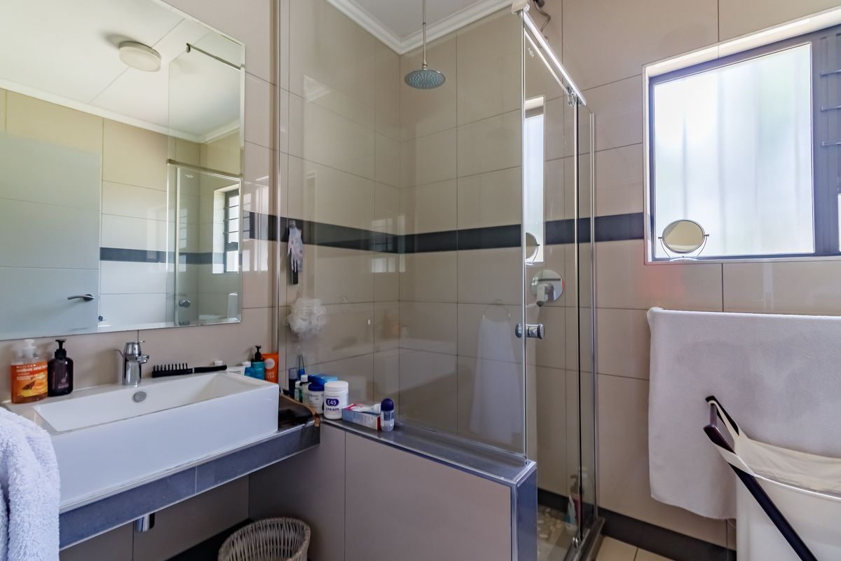 Modern bathroom featuring a glass-enclosed rainfall shower, wall-mounted basin with chrome fixtures, and neutral tiled walls with a decorative accent border.