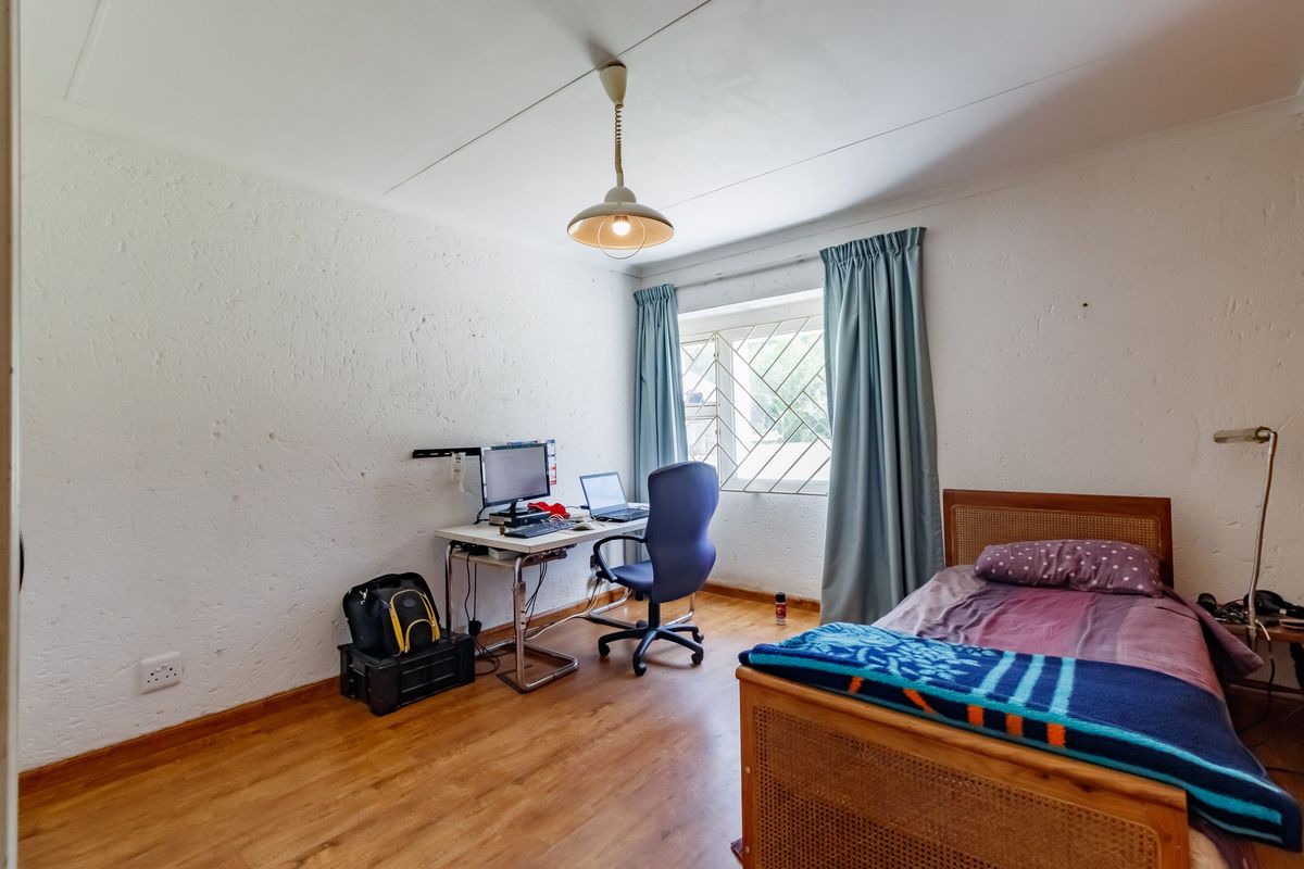 A functional bedroom featuring laminate flooring, a window with security bars, and a central pendant light fixture.