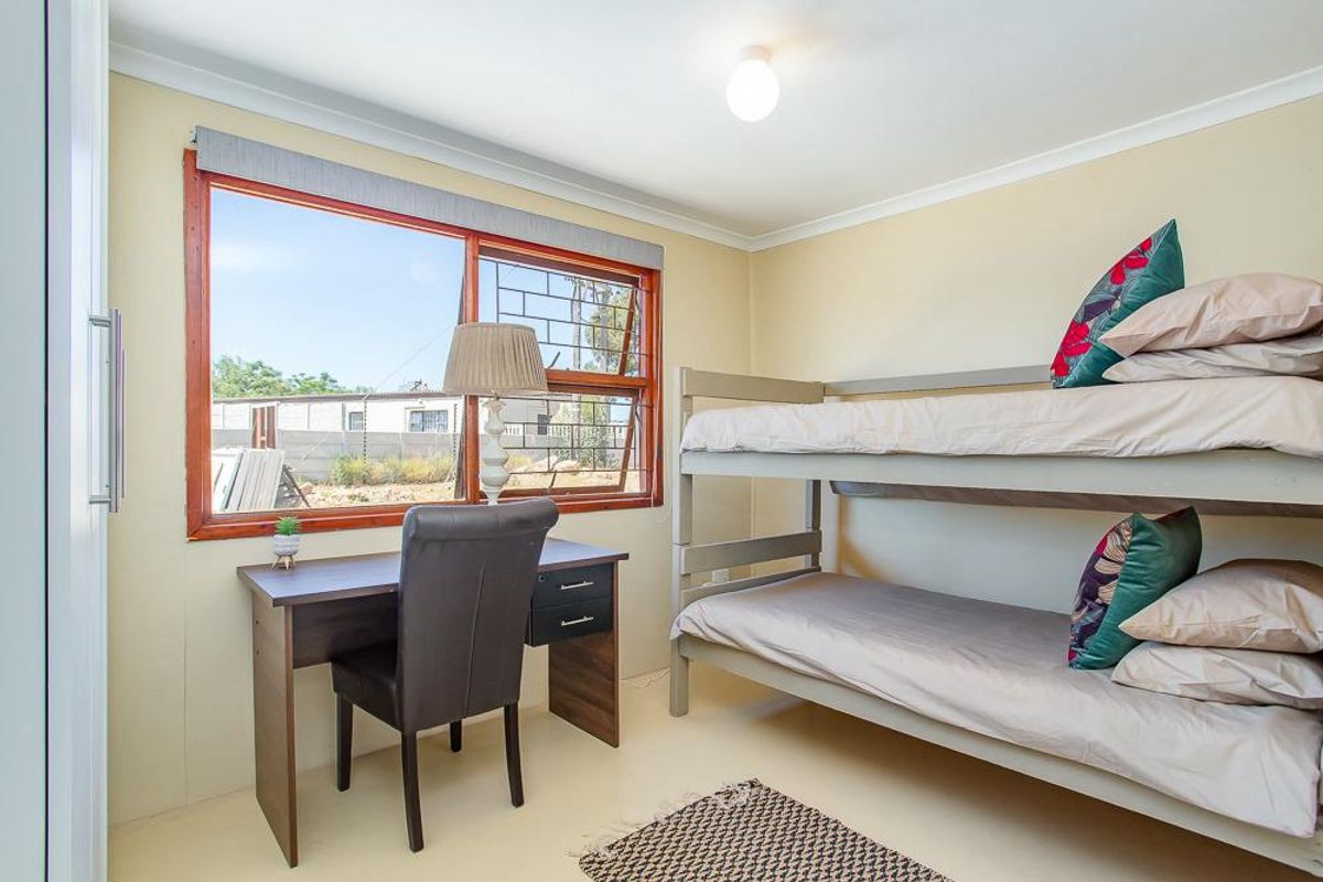 A functional bedroom featuring a timber-framed window with security bars, coved ceiling, and a built-in cupboard.