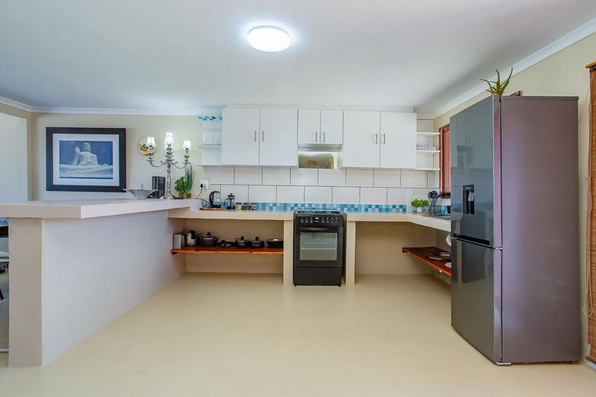 A functional kitchen featuring white cabinetry, a tiled backsplash, a breakfast bar, and a freestanding oven with an integrated extractor fan.