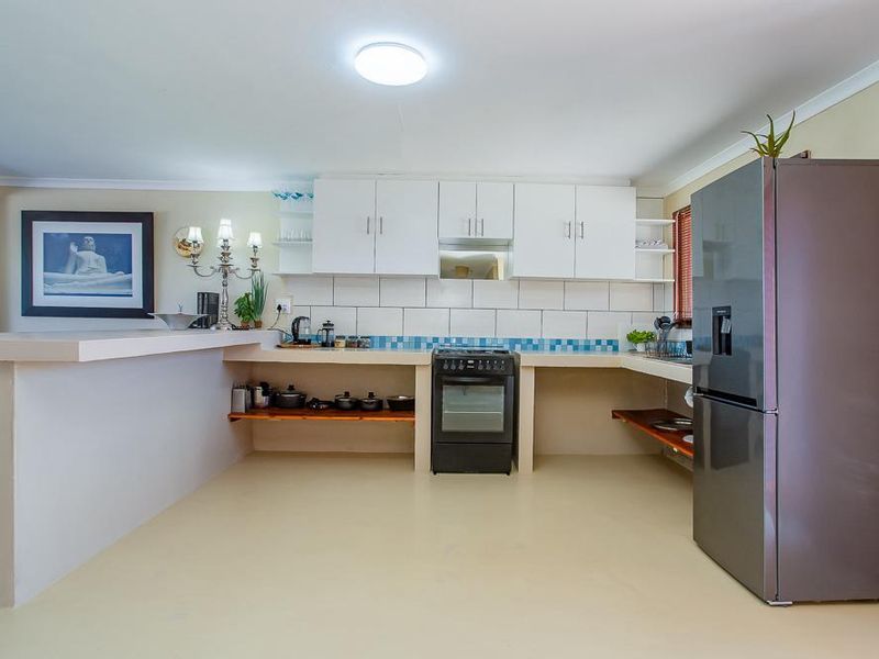 A functional kitchen featuring white cabinetry, a tiled backsplash, a breakfast bar, and a freestanding oven with an integrated extractor fan.