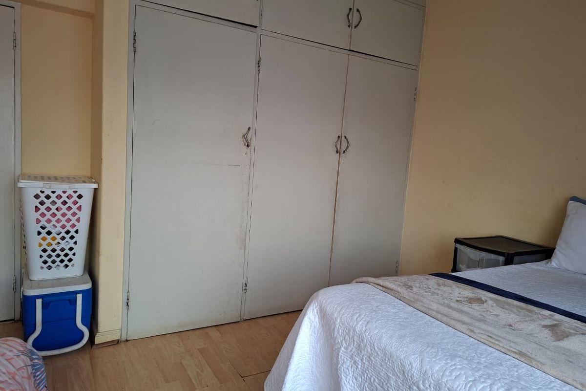 A bedroom featuring built-in floor-to-ceiling cupboards and light-toned laminate flooring.