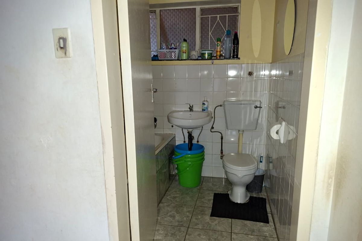 A compact bathroom featuring a standard toilet, wall-mounted basin, and tiled finishes, requiring modernization and maintenance.