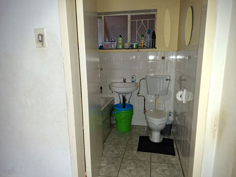 A compact bathroom featuring a standard toilet, wall-mounted basin, and tiled finishes, requiring modernization and maintenance.