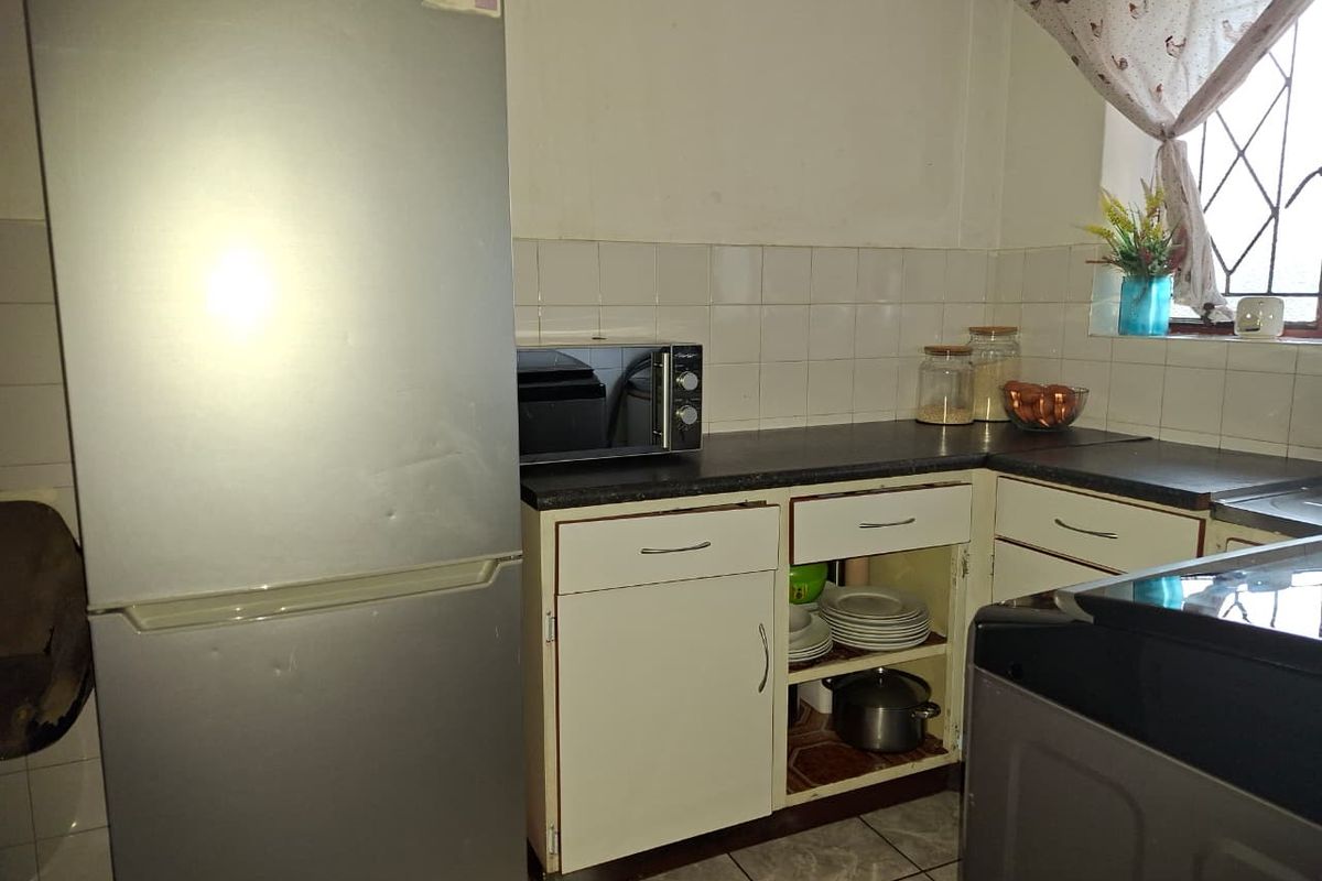 A compact kitchen featuring built-in cabinetry, tiled splashbacks, and a window with security bars, offering a functional layout for a small apartment.