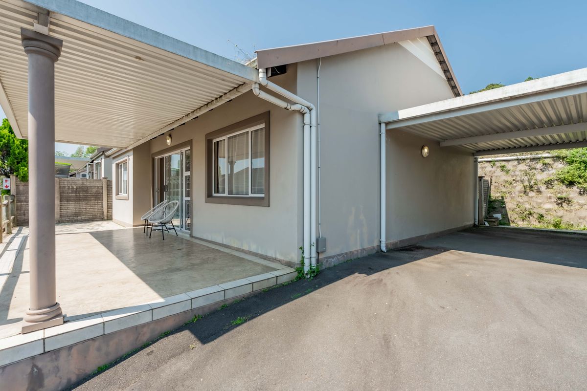Rear view of the townhouse featuring a covered patio area, adjacent carport, and paved driveway with access to the living space via sliding doors.