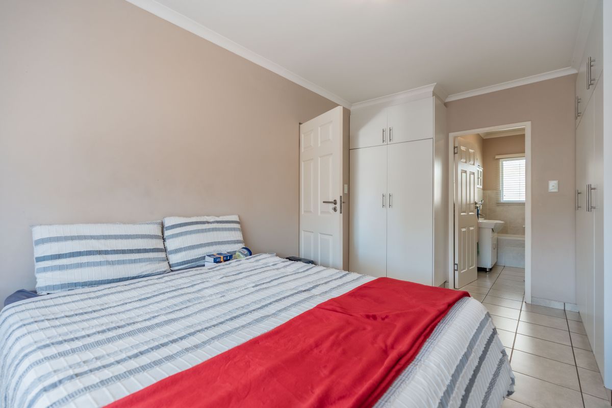 A well-maintained bedroom featuring built-in cupboards, tiled flooring, and direct access to an en-suite bathroom.