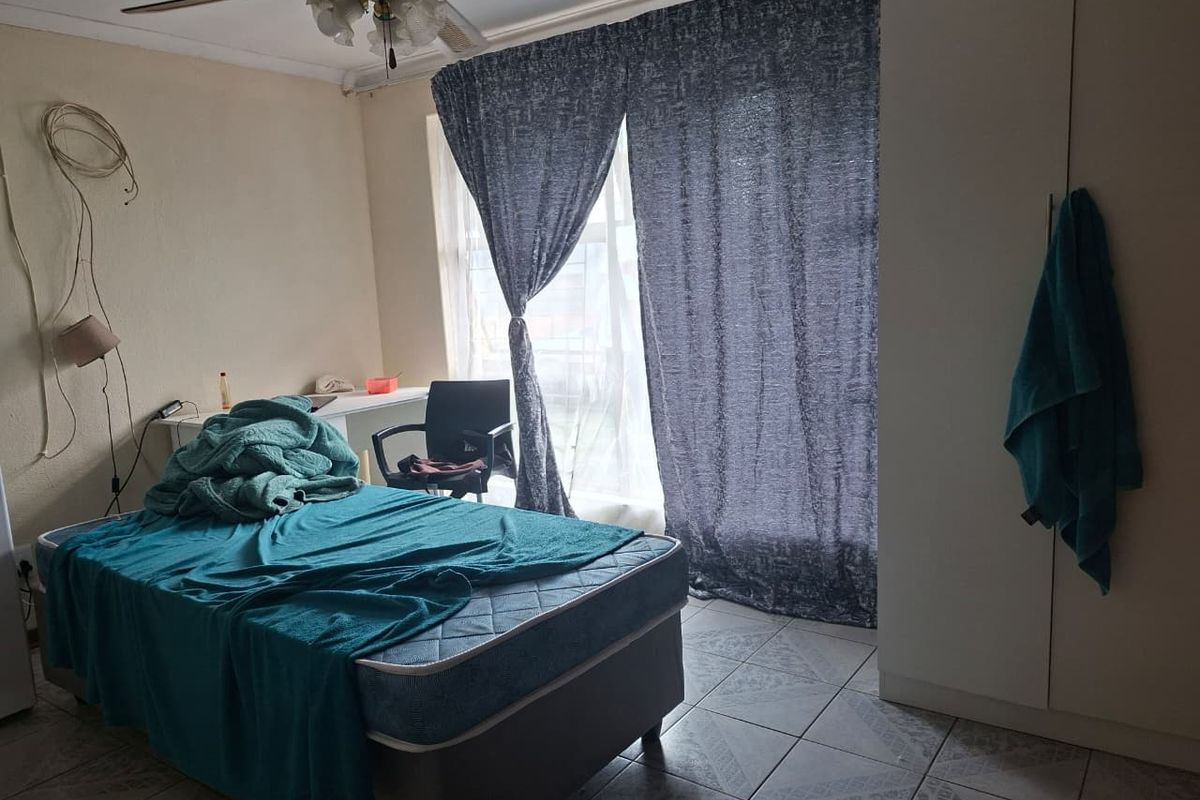 A bedroom featuring tiled flooring, a ceiling fan, and built-in wardrobe storage, with direct access to natural light through window curtains.