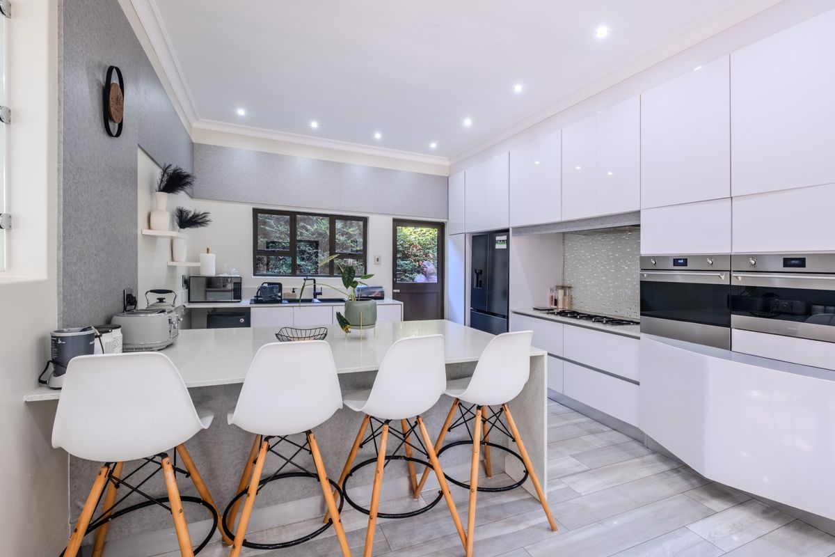 Modern kitchen featuring high-gloss cabinetry, quartz countertops, integrated appliances, and a central island with breakfast bar seating.
