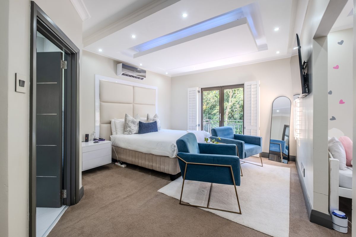 Spacious bedroom featuring a recessed ceiling with ambient lighting, split-system air conditioning, and plantation shutters opening to a balcony.