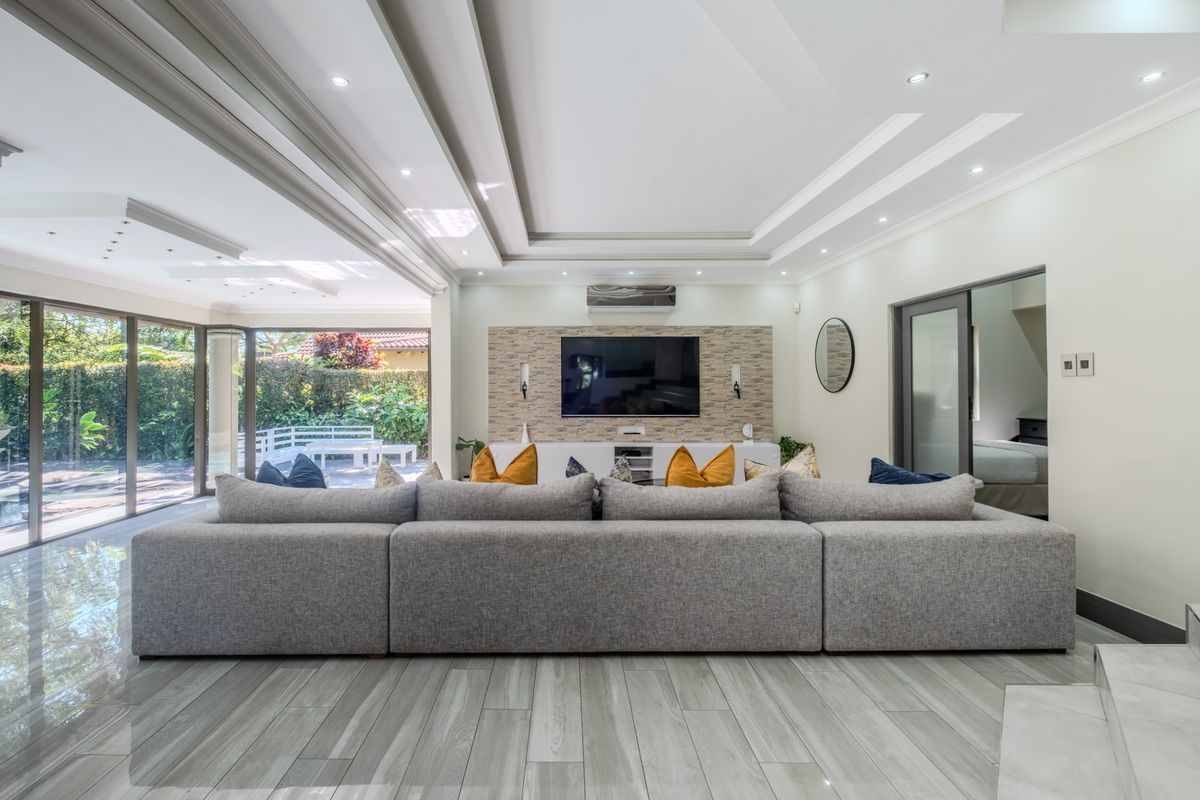 Spacious living room featuring a stone feature wall, recessed ceiling with downlights, split-system air conditioning, and large sliding glass doors opening to the garden.