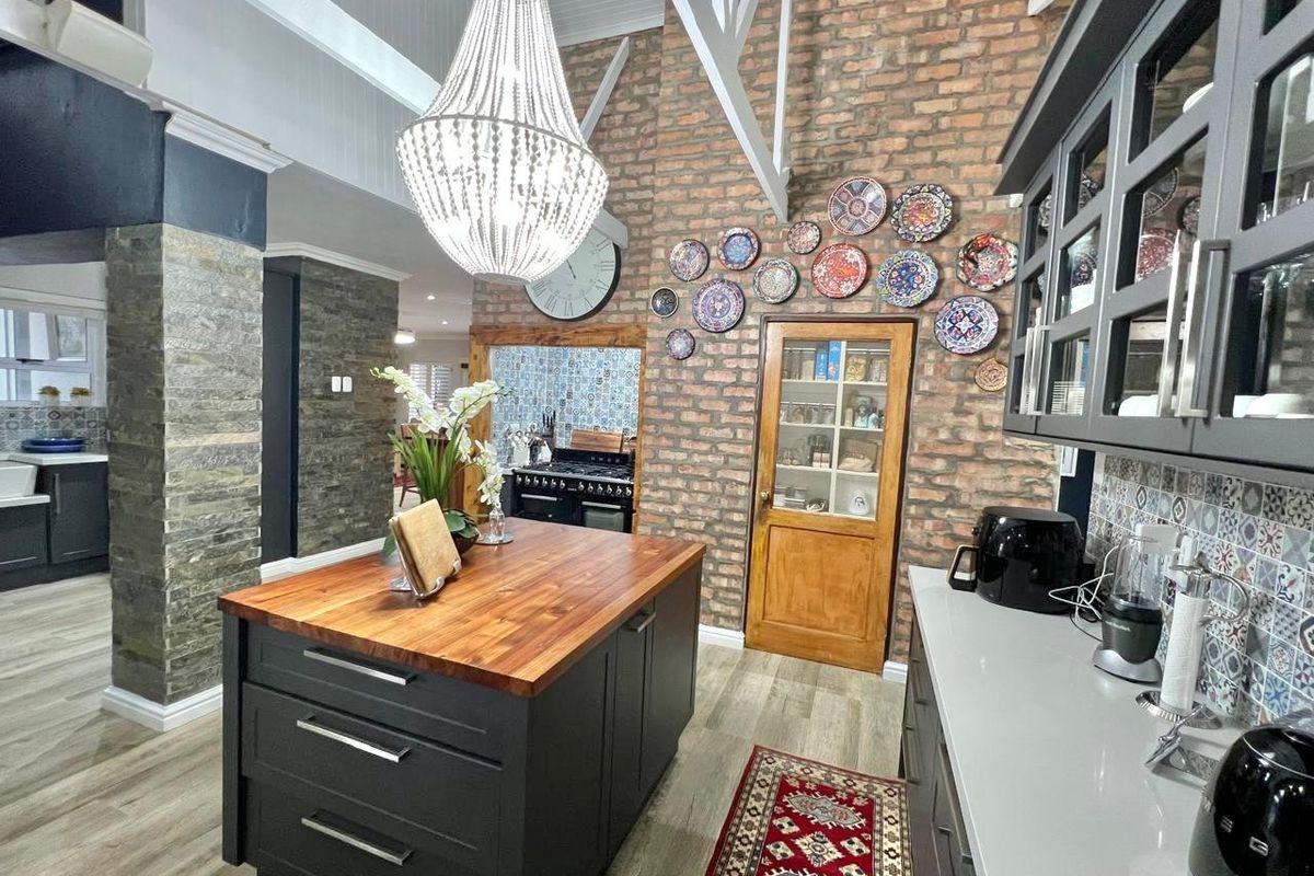 A stylish kitchen featuring a central island with a wooden countertop, exposed brick walls, and a vaulted ceiling with exposed trusses.