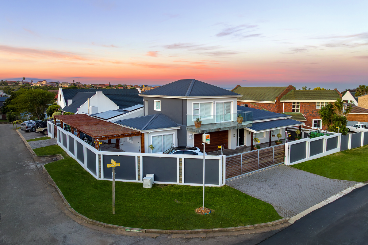 Aerial view of a modern two-story house featuring a metal roof, solar panels, timber pergola, and secure perimeter wall with electric fencing.