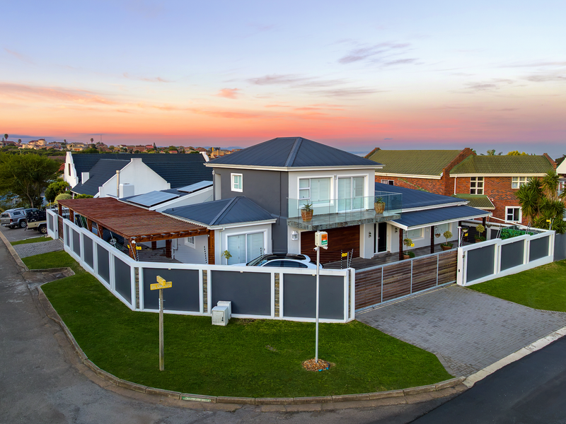 Aerial view of a modern two-story house featuring a metal roof, solar panels, timber pergola, and secure perimeter wall with electric fencing.