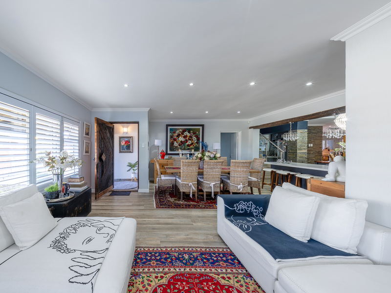 Spacious open-plan living and dining area featuring timber-look flooring, recessed lighting, a breakfast bar, and plantation shutters, creating a bright and inviting atmosphere.
