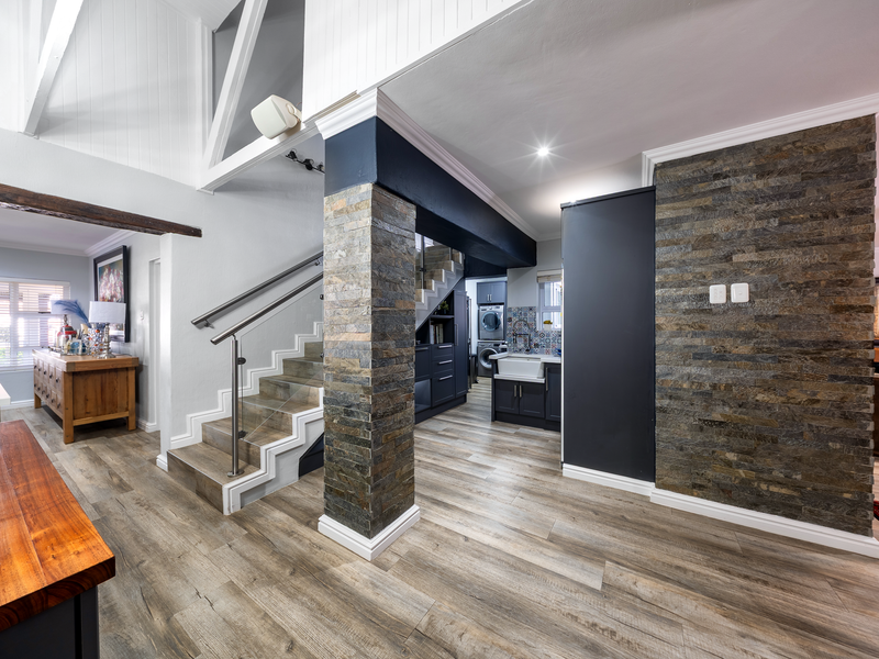 Modern open-plan living area featuring a striking stone-clad pillar, vaulted ceilings with exposed beams, and a contemporary staircase with glass balustrades.