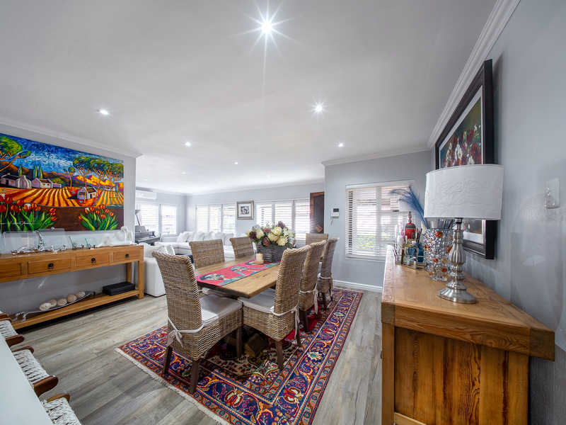 Spacious open-plan dining and living area featuring modern laminate flooring, recessed downlighting, and large windows with venetian blinds.