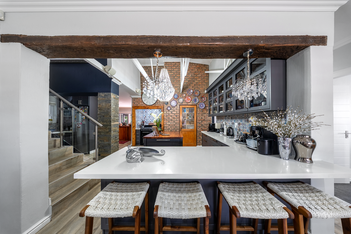 Modern kitchen featuring a large quartz breakfast bar, exposed brick feature wall, and elegant glass-fronted cabinetry, seamlessly connected to an open-plan living area.
