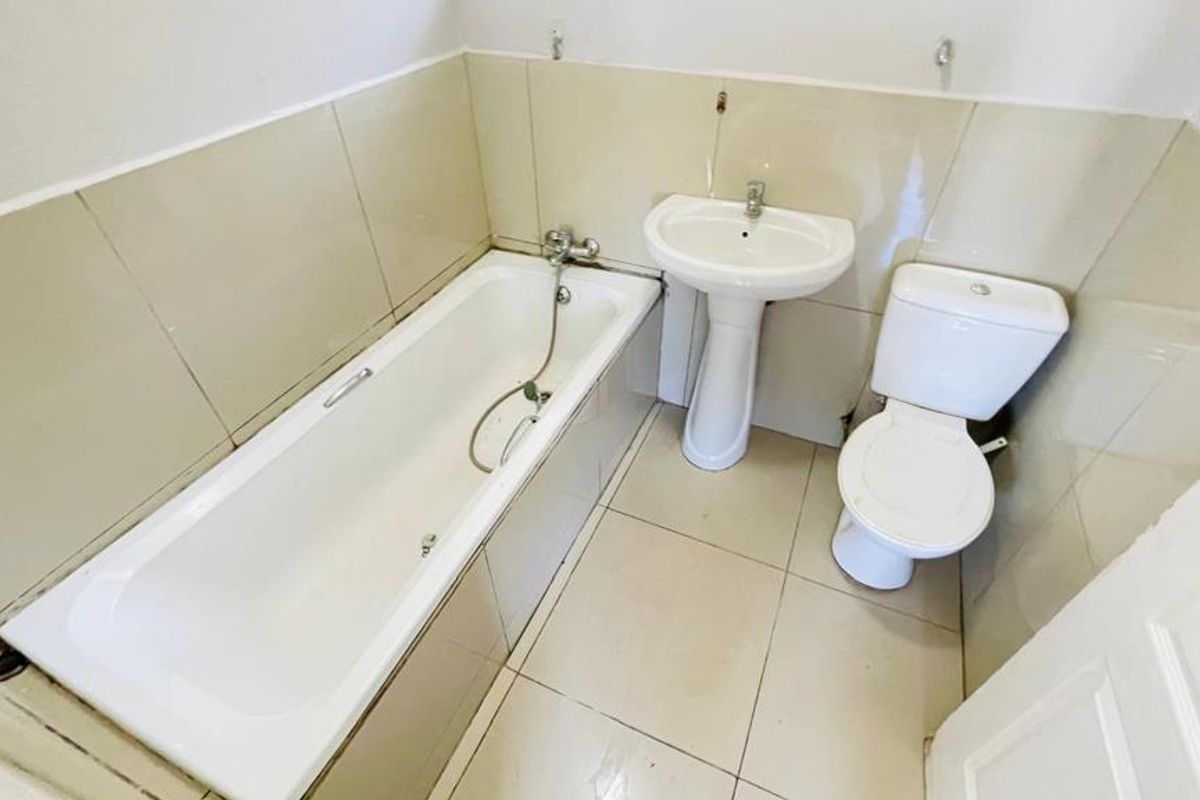 A functional bathroom featuring a standard bathtub, pedestal basin, and toilet with neutral wall and floor tiling.