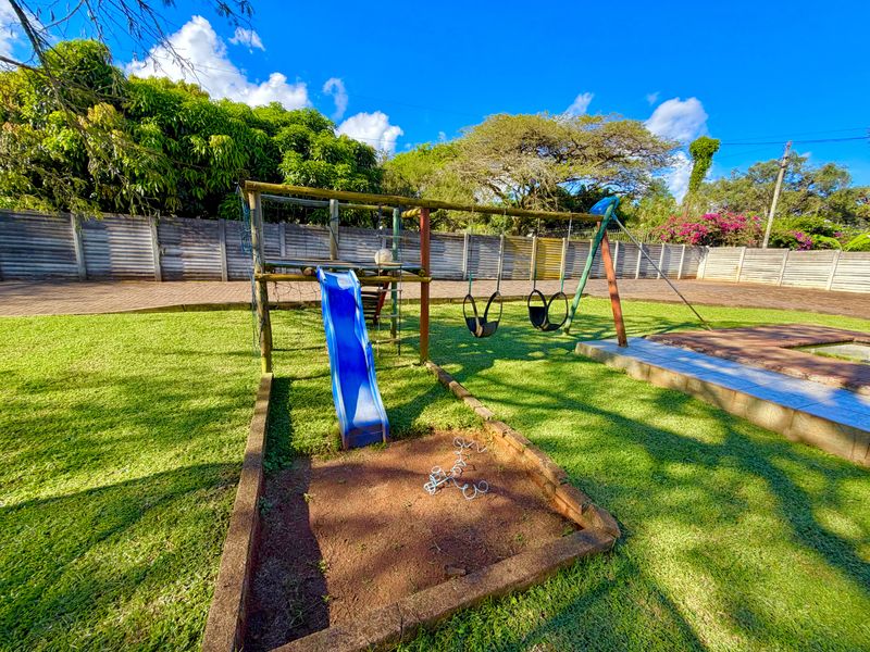 A spacious garden area featuring a lawn, paved driveway, concrete perimeter wall, and existing playground equipment.